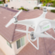 A white drone flying over a brown house